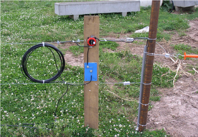 two series of straight wires are attached to a central wooden post, with a coil of wires attached between the two electrical wires